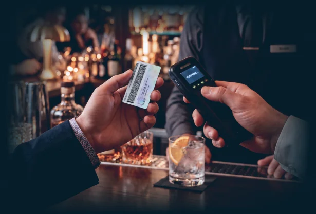 A bartender scanning a customer's driver's license with a handheld device at a cocktail bar.