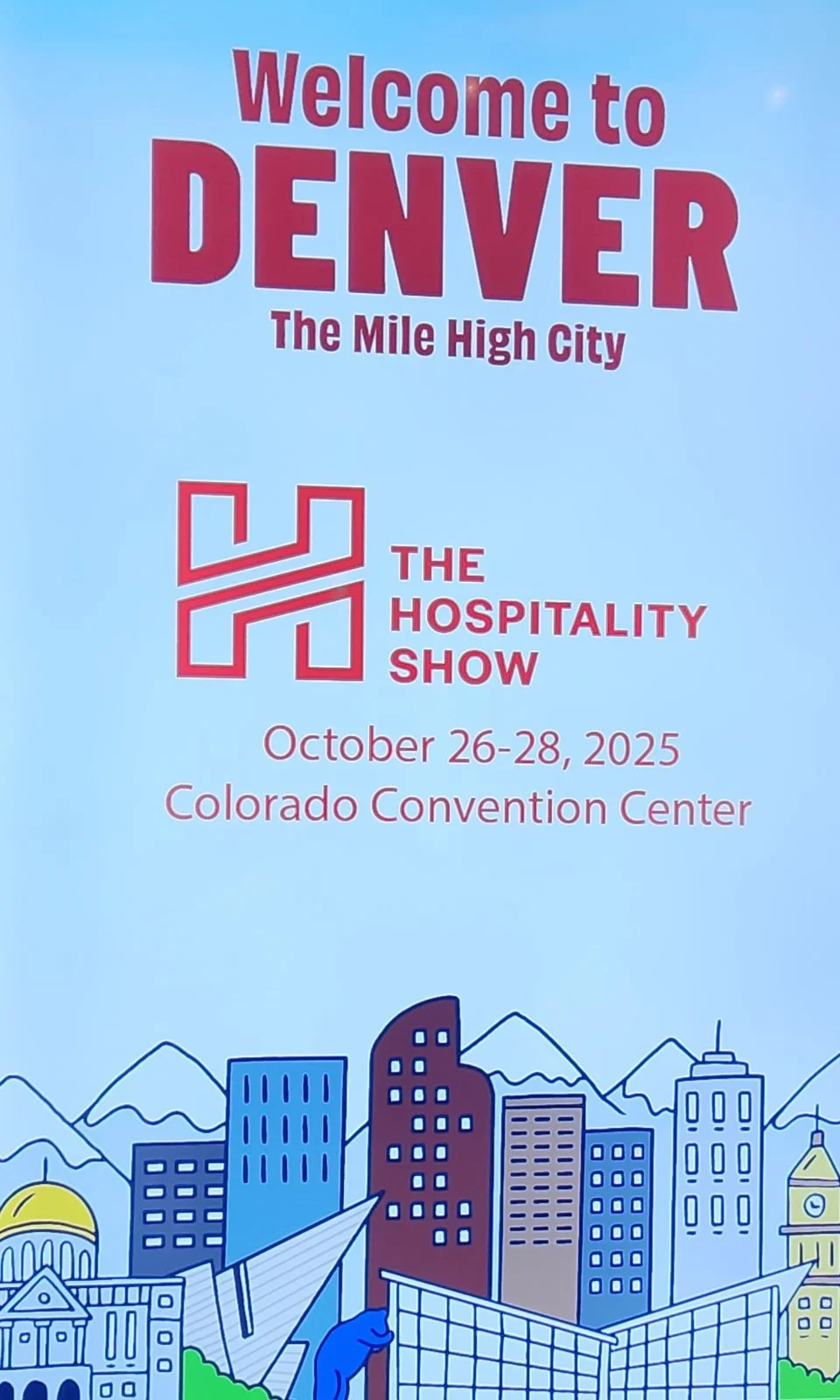 Welcome to The Hospitality Show 2025: Denver's Mile High City at Colorado Convention Center Official welcome banner for The Hospitality Show 2025, October 26-28 at Colorado Convention Center in Denver, featuring bold red text "Welcome to DENVER The Mile High City" and event logo, with illustrated skyline of mountains, high-rises, and blue bear sculpture on a blue background.