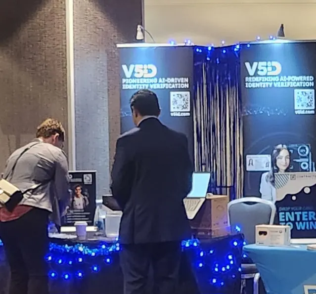 V5iD CTO in suit interacting with an attendee at the company's booth during the Oregon Banking Leadership Symposium 2025 in Portland, featuring banners on pioneering and redefining AI-driven identity verification, QR codes to v5id.com, blue lighting, laptop