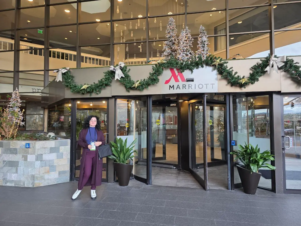 V5iD CEO standing and smiling outside the festively decorated Marriott hotel entrance in Portland during the Oregon Banking Leadership Symposium 2025, with holiday garlands, lighted Christmas trees, bows, revolving glass doors, and potted plants