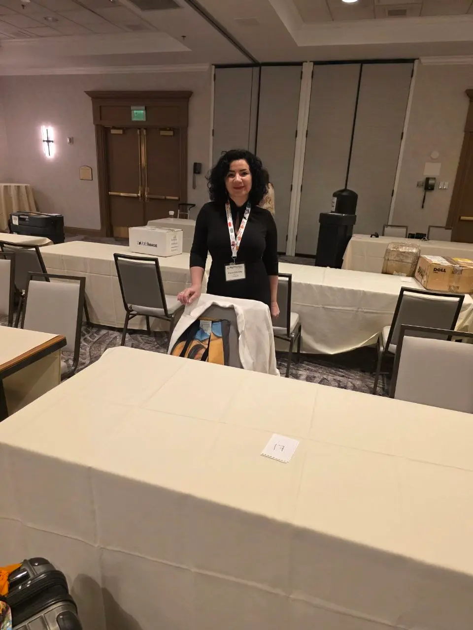 V5iD® CEO standing in the exhibit room at the SymWest conference, wearing a lanyard and badge, waiting for booth equipment to be delivered to the setup area