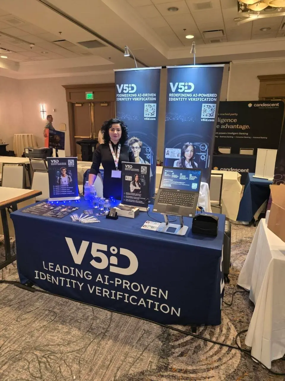 V5iD® CEO standing in front of a fully set up and ready-to-go V5iD booth at the SymWest conference, with branded banners, laptops, and promotional materials displayed
