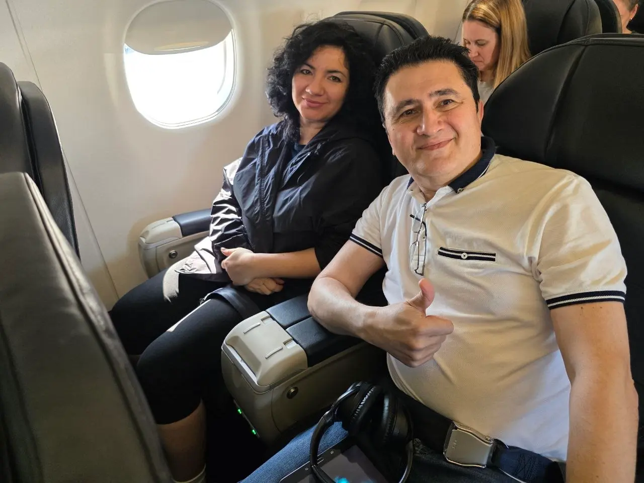 V5iD CTO and CEO seated on an airplane flying home to Portland from Salt Lake City, with the CTO giving a thumbs-up gesture and the CEO smiling from the window seat after the SymWest 2026 conference