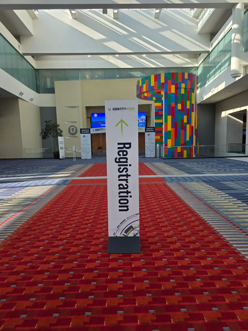 Tall Identity Week America registration sign in the main hall of Walter E. Washington Convention Center with colorful modern sculpture in the background