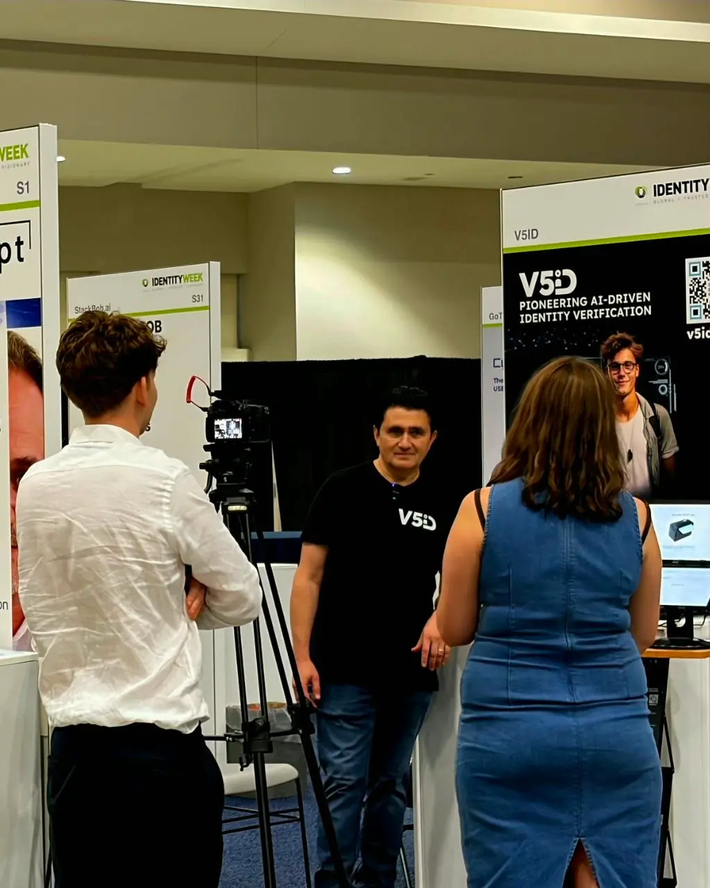 V5iD team member being filmed during an interview at the company booth while discussing AI-driven identity verification solutions at Identity Week America 2026