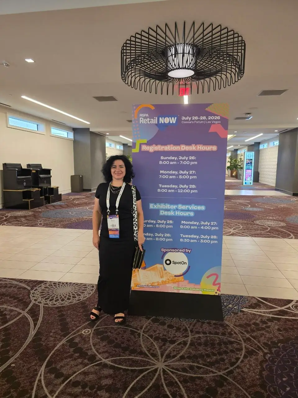 V5iD CEO with RSPA RetailNOW 2026 event poster at Caesars Forum Las Vegas V5iD CEO standing next to a large RSPA RetailNOW 2026 poster showing registration and exhibitor services desk hours inside Caesars Forum, Las Vegas, July 26-28, 2026.